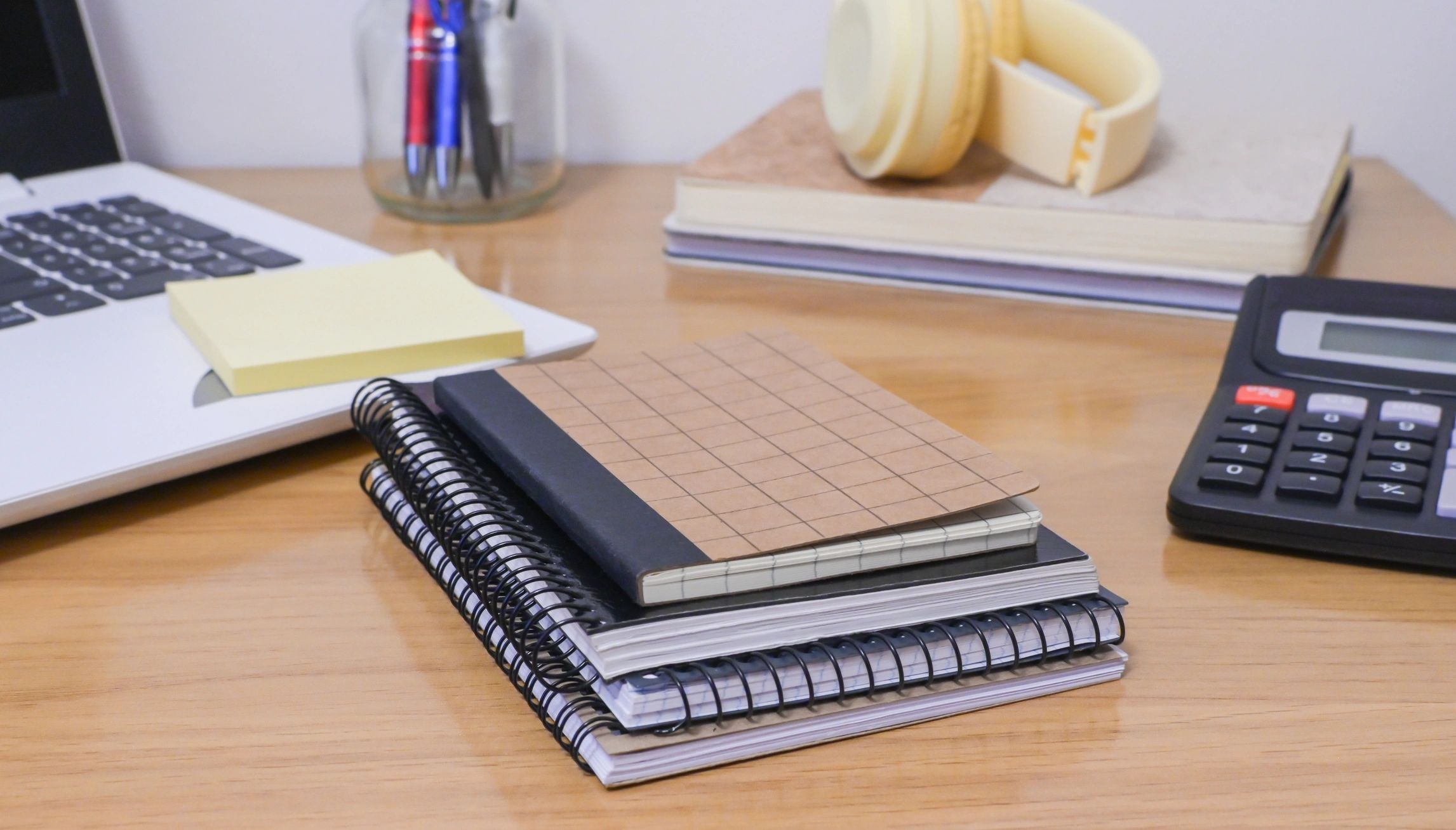 Office desk setup with a laptop, calculator, notebooks, and pens, representing a productive environment for finance, accounting, and expense management